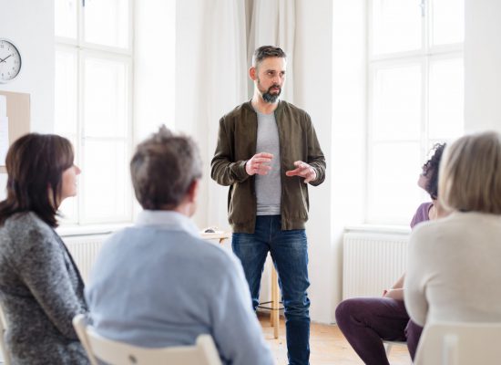 A mature man standing and talking to other people during group therapy.