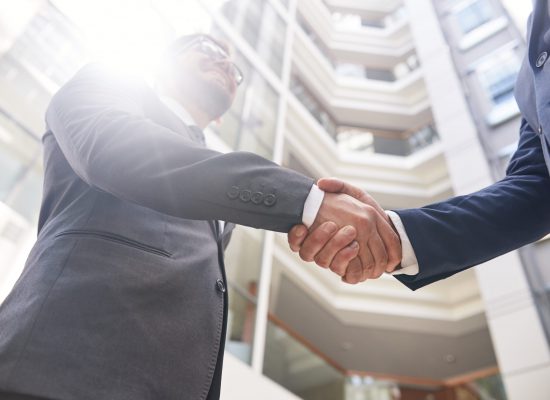 Low angle view of unrecognizable businessmen shaking hands after successful completion of negotiations, lens flare