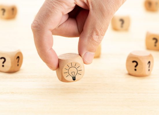 Creative idea or innovation concept. Hand picked wooden cube block with question mark symbol and light bulb icon on wood table