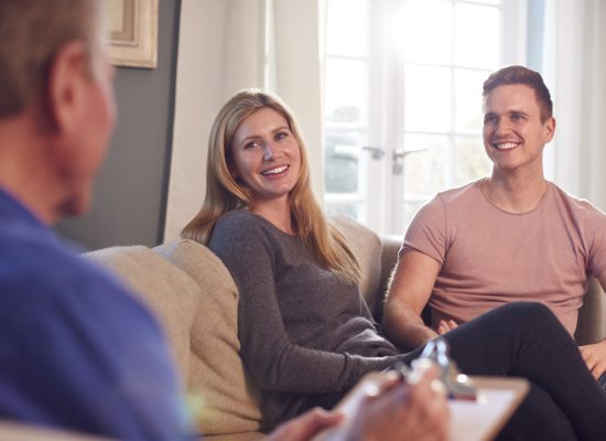 Male Social Worker With Clipboard Visiting Young Couple At Home