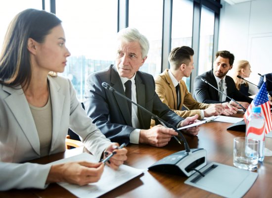 Pensive confident representative of governments advising each others while analyzing information on papers, they sitting in a row at table