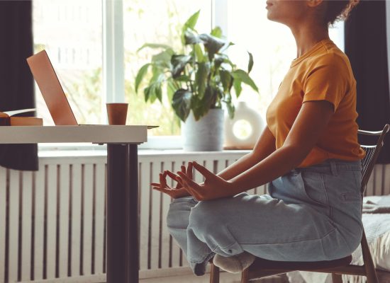 Stress relief during freelance work. Cropped photo of african american woman freelancer sitting in lotus pose and meditating with hands in mudra gesture on chair in front of open laptop on table